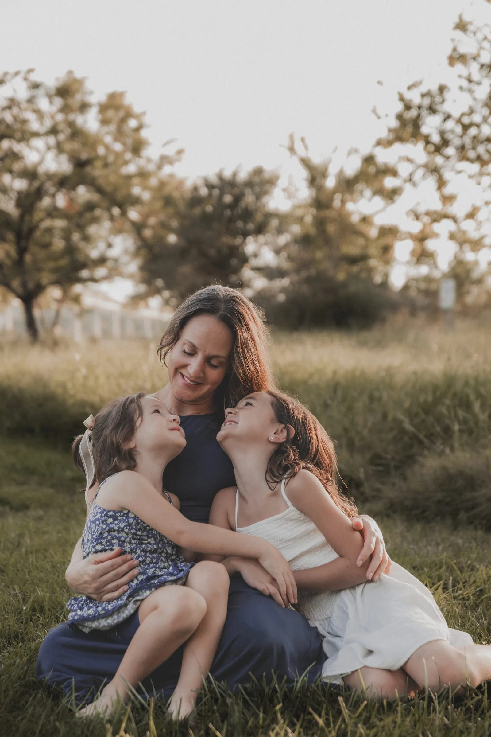 Two little girls sitting in the grass, gazing up at their smiling mom