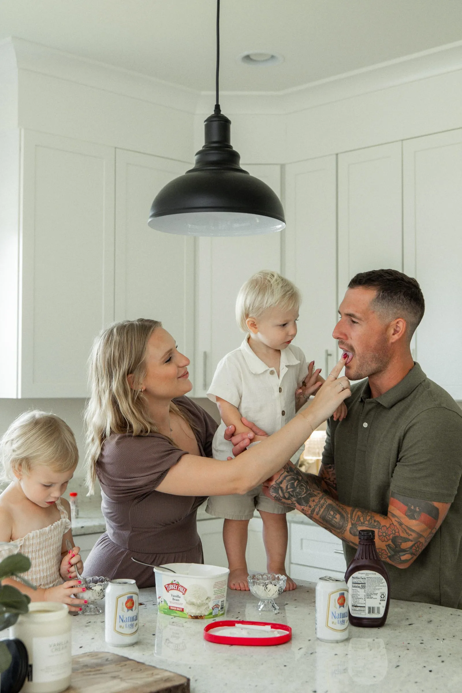 Mom sneaking a taste of frosting to dad while the kids help bake in the kitchen