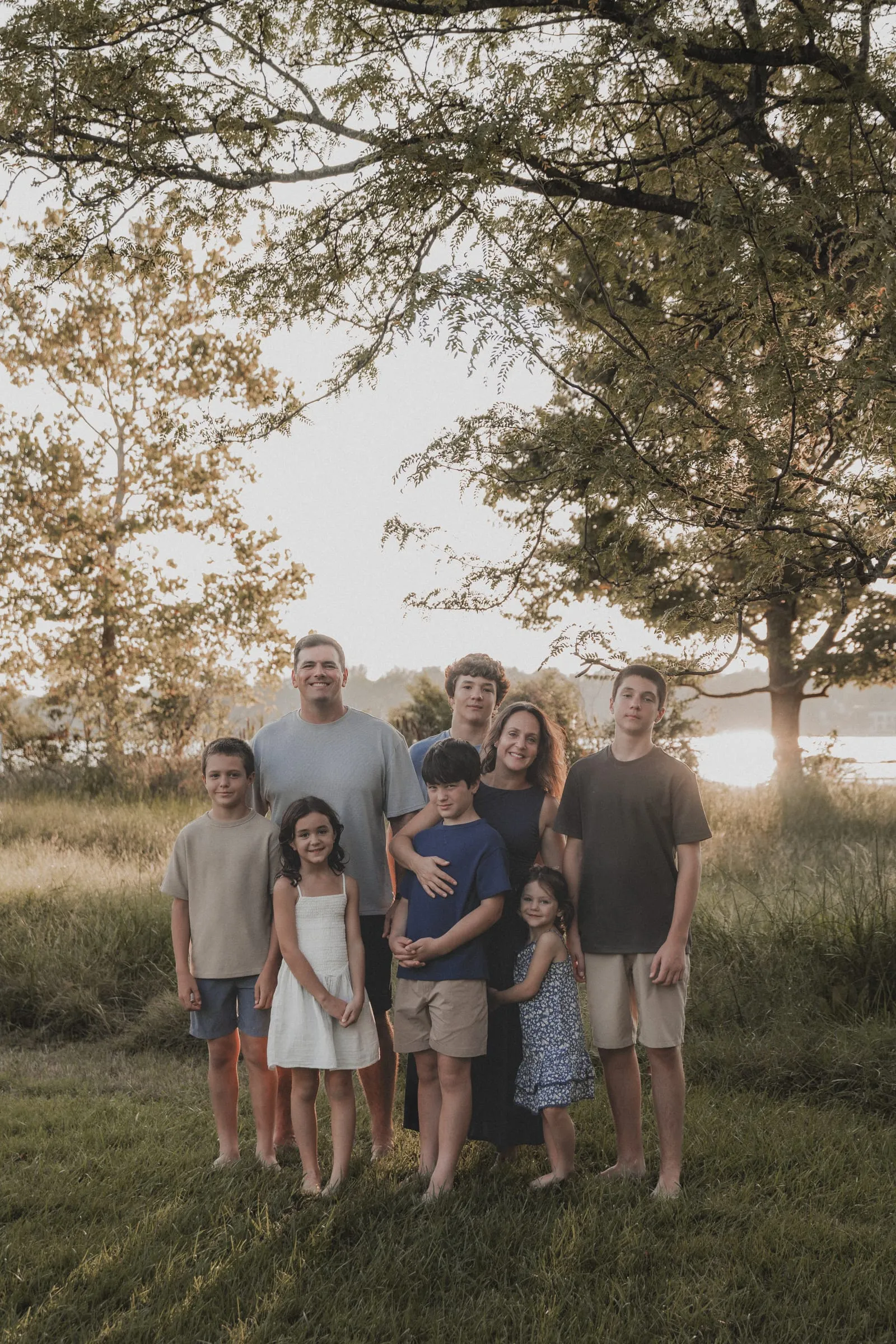 A big family of eight standing together in golden light by the water