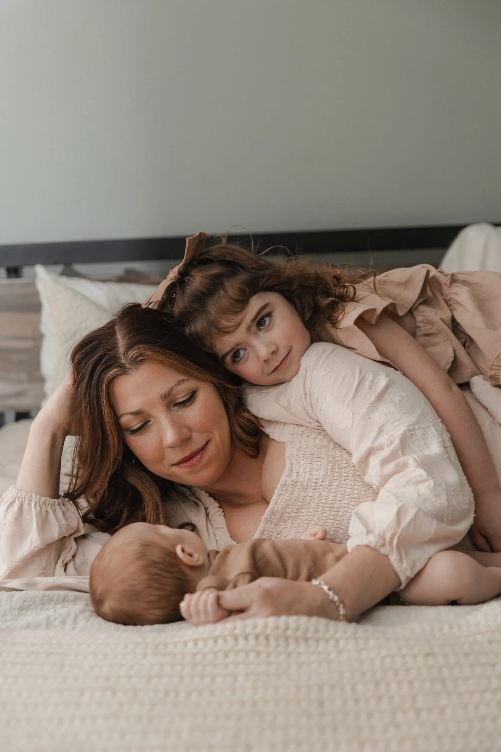 A mom and her little girl snuggled on the bed beside their newborn