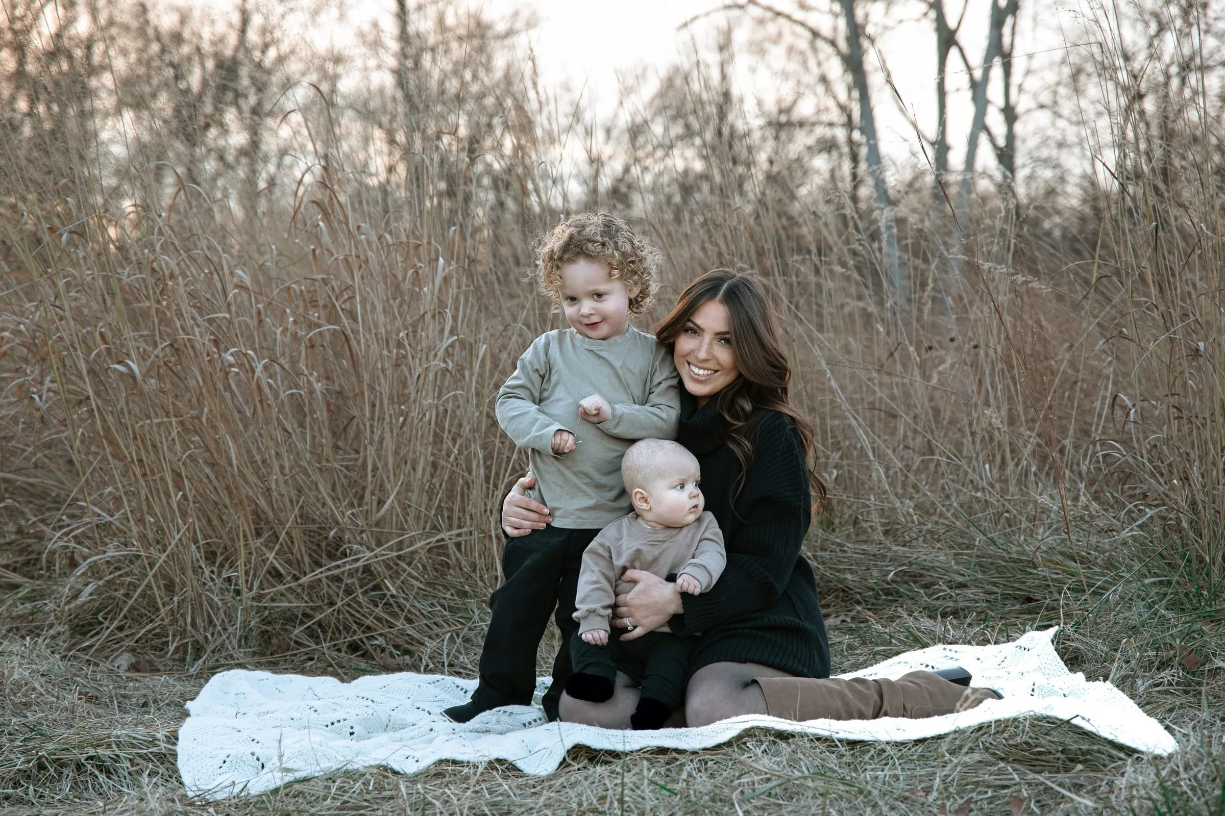 Brittany with her two boys on a cream blanket in tall grass