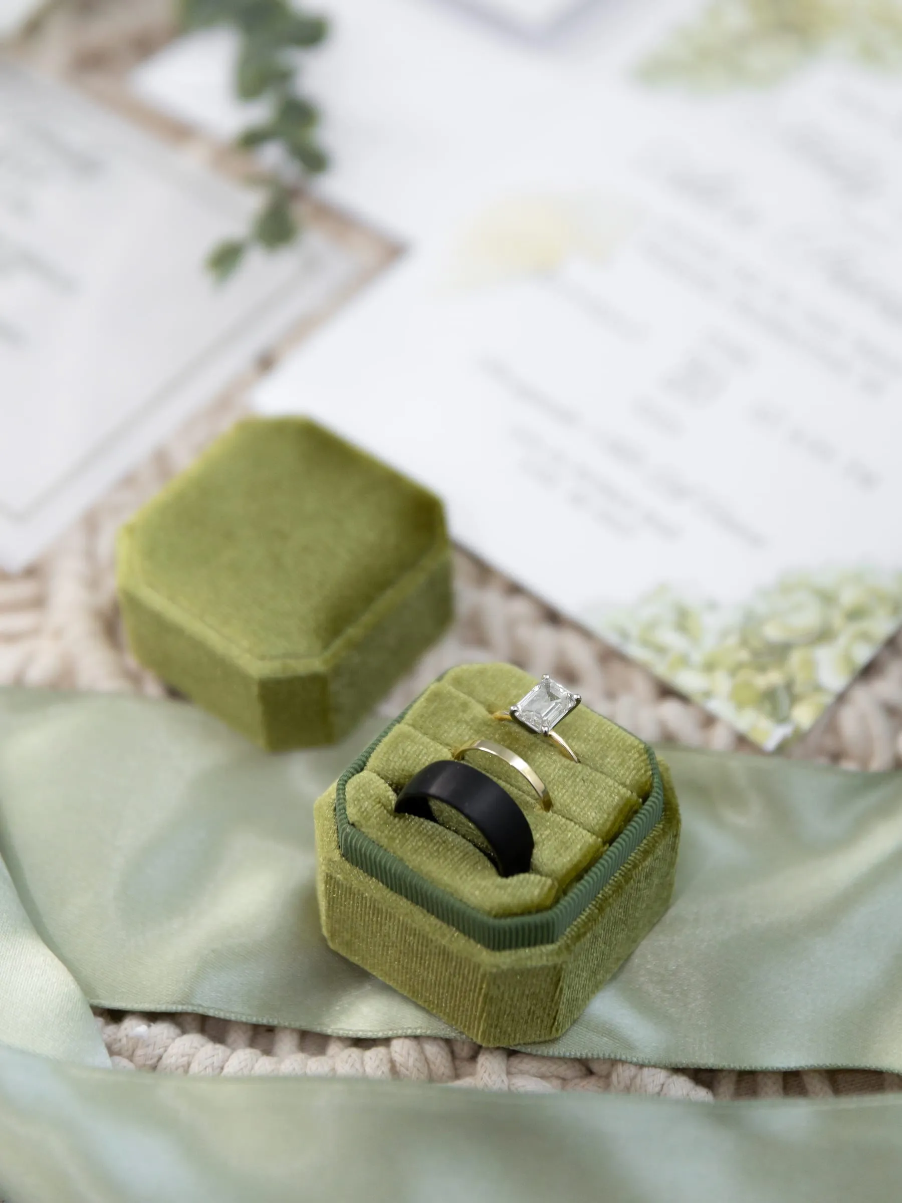 Wedding rings in a sage velvet ring box beside the invitation suite
