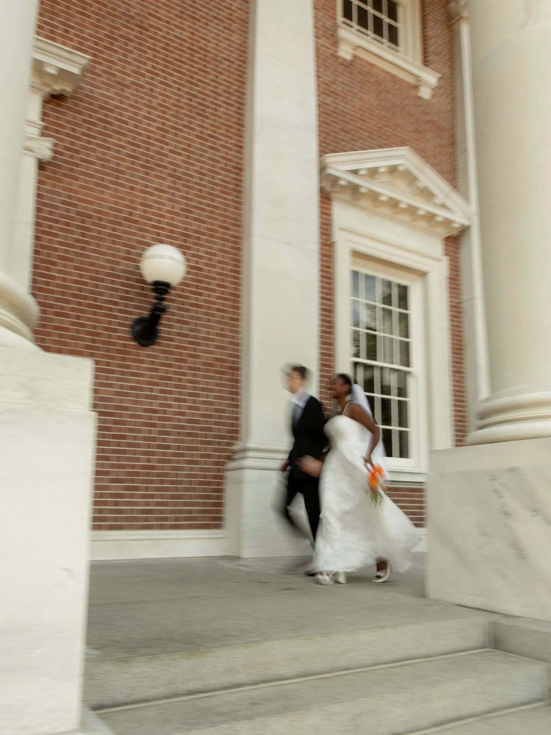 Newlyweds running hand in hand down the steps of a brick venue