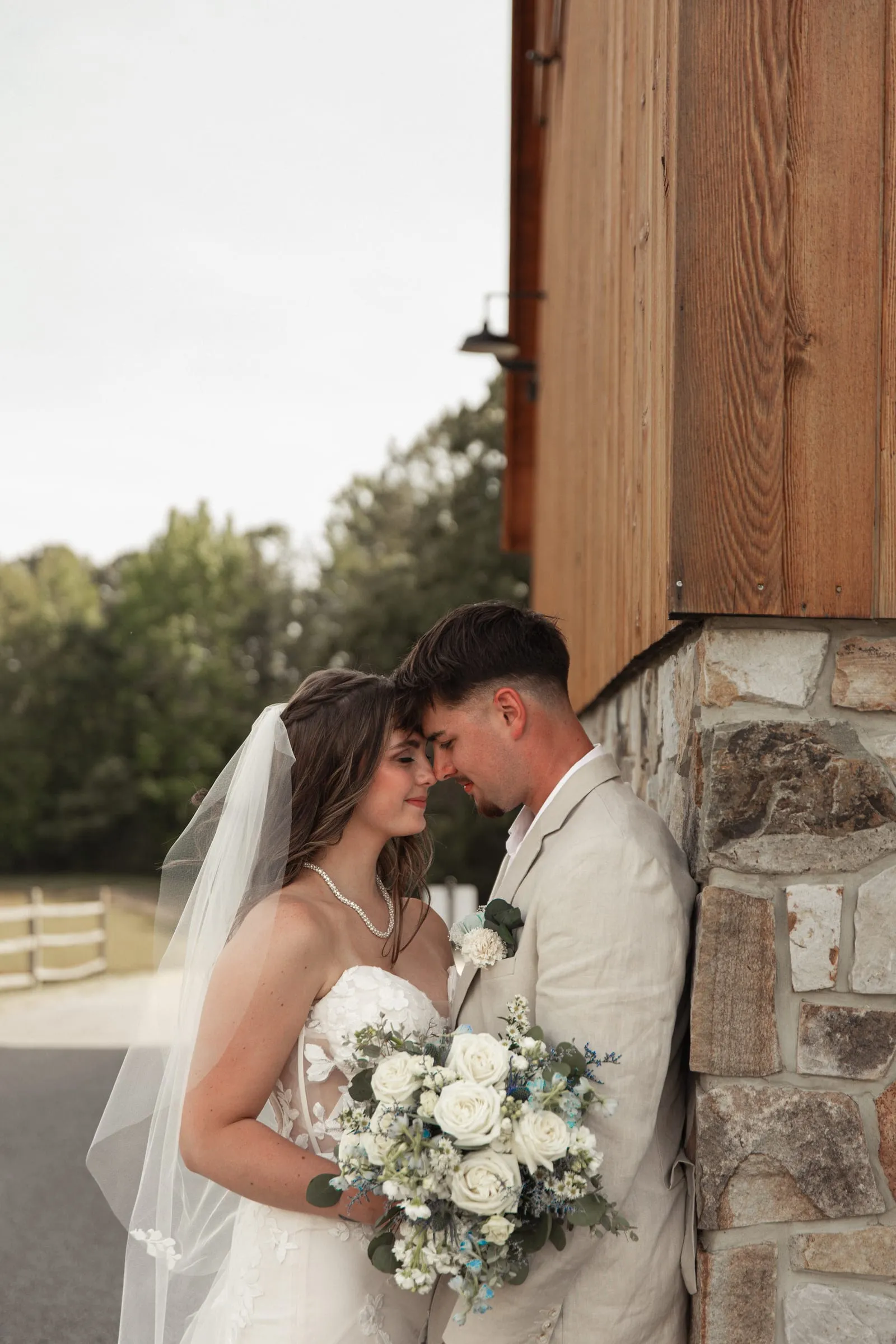 A bride and groom leaning in close beside a stone and timber barn