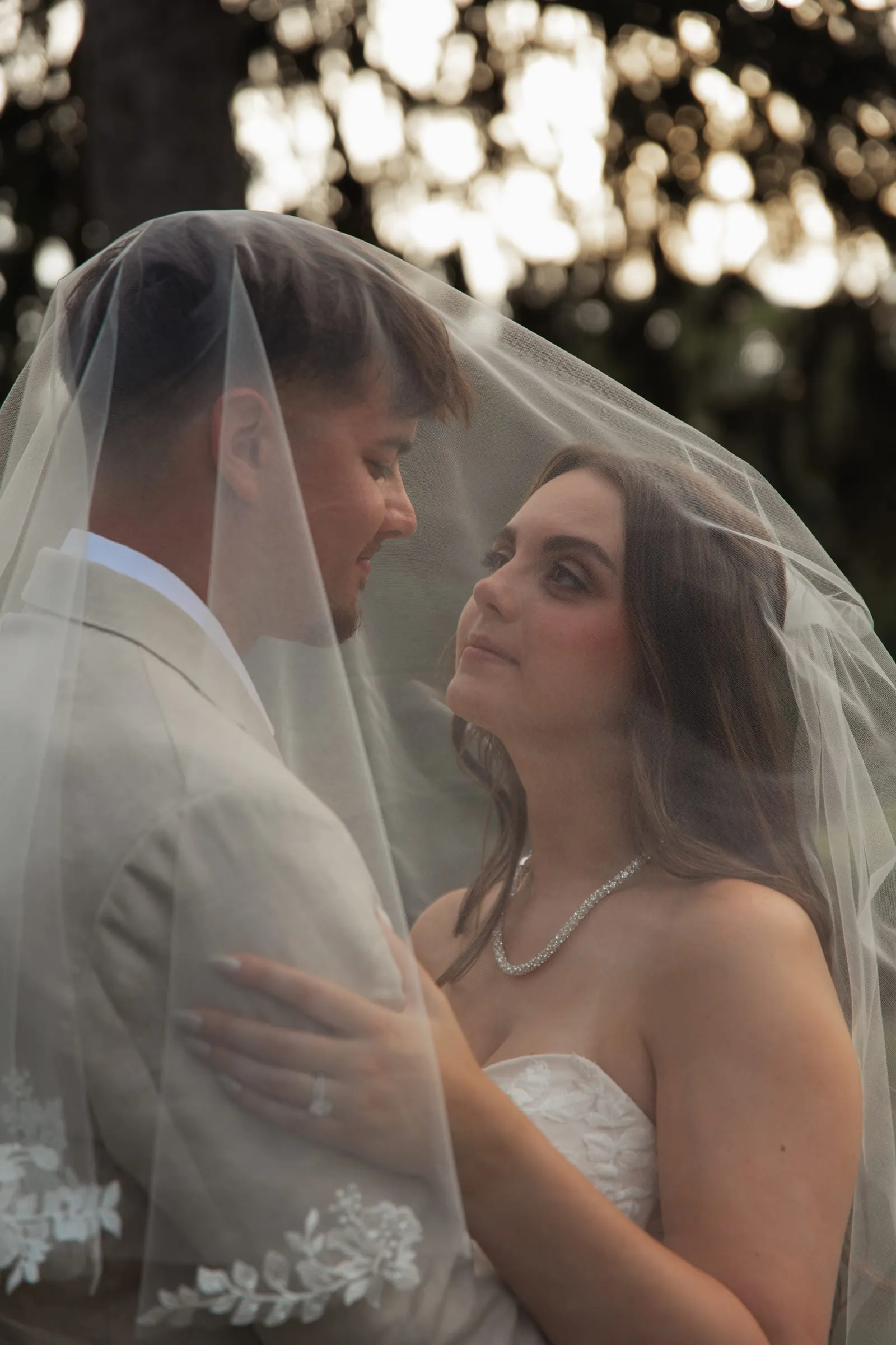 Bride and groom close together beneath her veil at golden hour