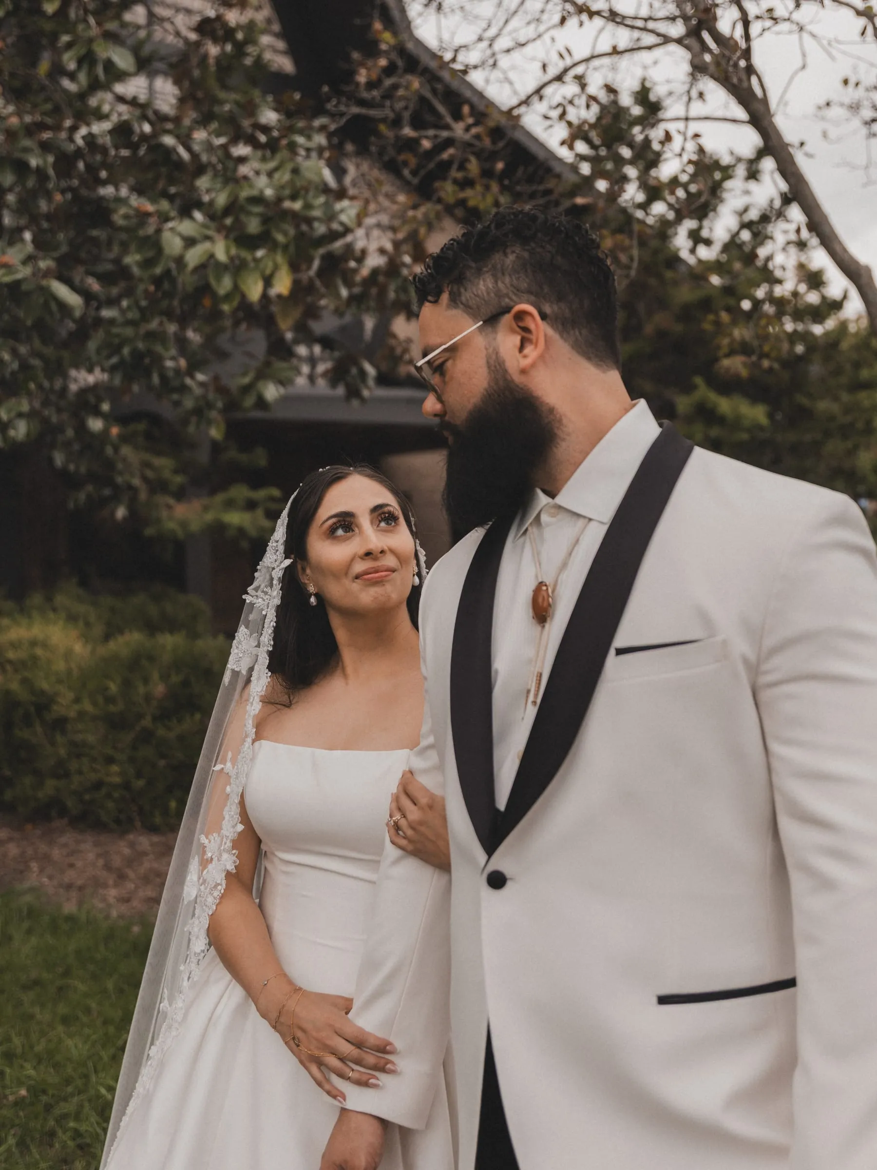 A bride in a lace veil smiling up at her groom in the church garden